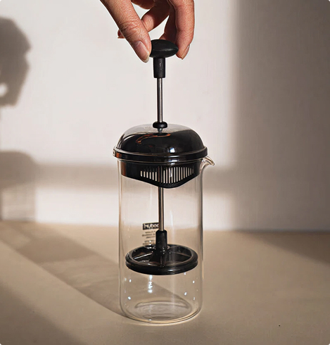 Main actionnant une cafetière à piston en verre avec couvercle noir